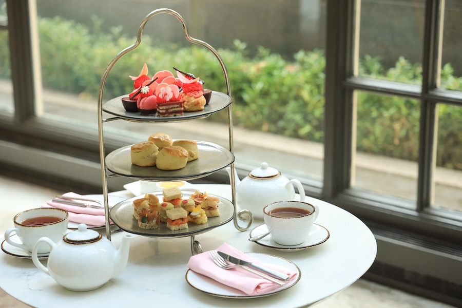 An afternoon tea spread including a three-layer display topped with small, pink pastries. 