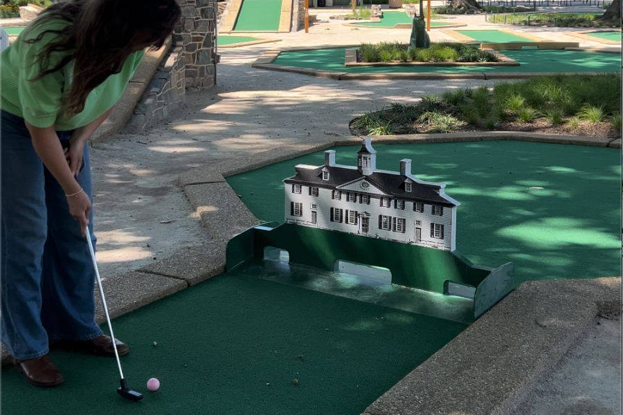 A woman lines up a shot at an outdoor mini golf course in East Potomac Park, featuring a playful obstacle modeled after a historic building.