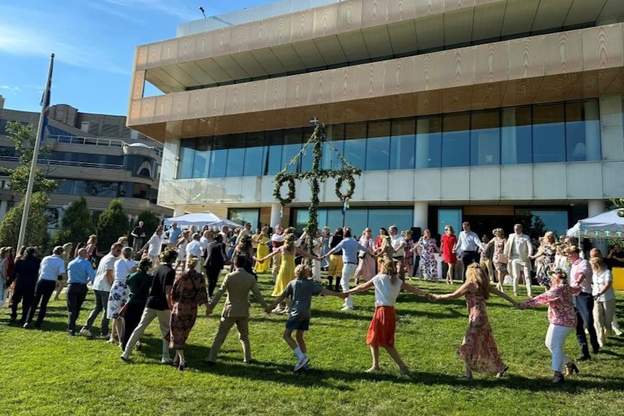 People dressed in festive summer attire dance around a decorated maypole during a traditional Midsummer celebration on the lawn of House of Sweden in Washington, DC.