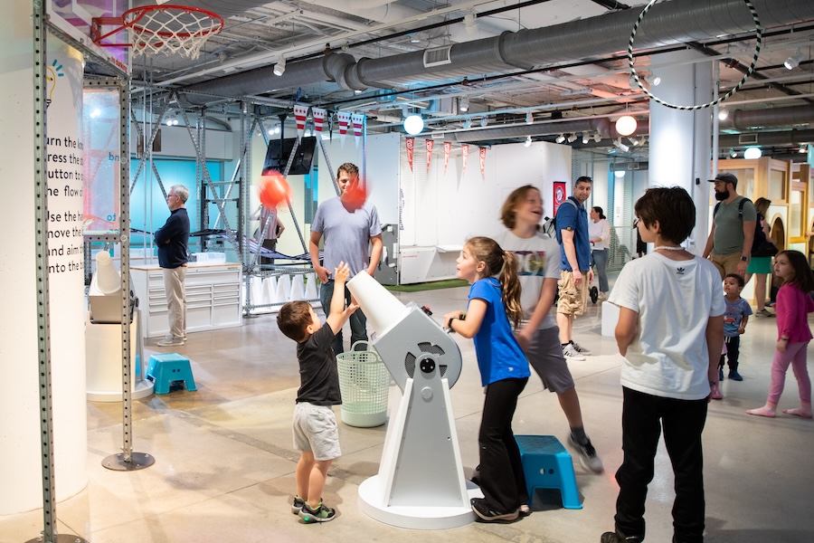 Children excitedly play with a balloon and a fan as part of an interactive museum exhibit. 