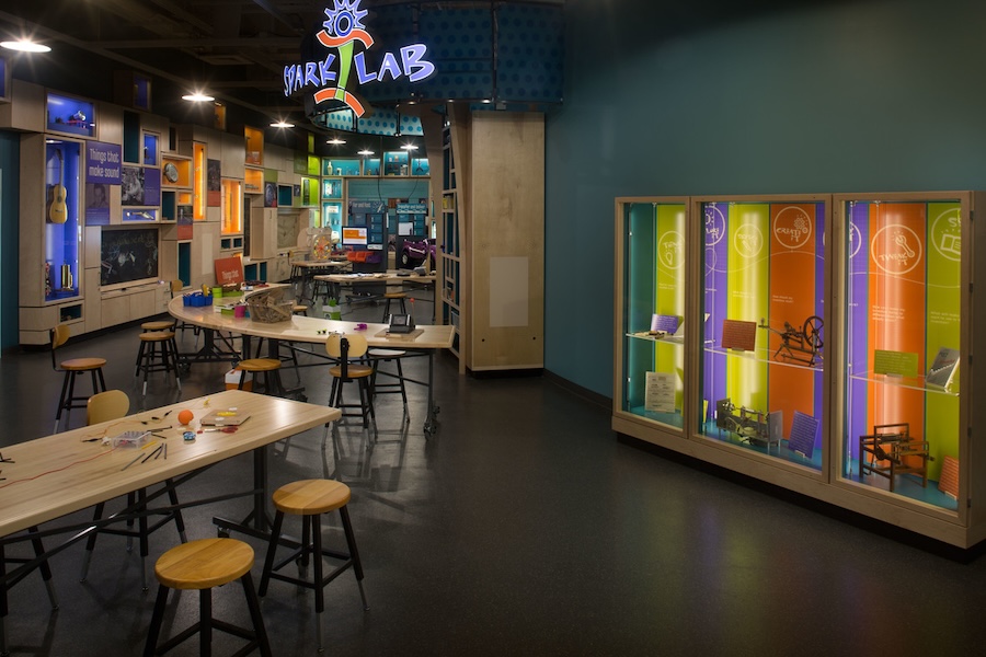 Colorful, hands-on activity area at Spark!Lab featuring tables, stools and vibrant display cases.