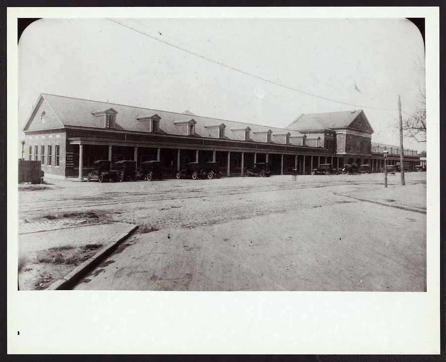 Black-and-white photo of a historic building in Washington, DC, with early automobiles parked along the street.