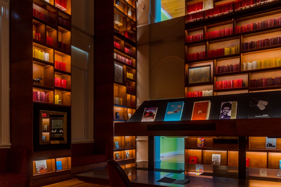 A warmly lit reading room at Planet Word Museum features colorful book displays and illuminated shelves filled with books organized by hue.