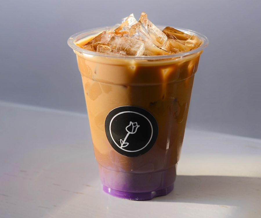 A professional photo of an iced coffee drink with a rose sticker and purple ube syrup visible at the bottom.