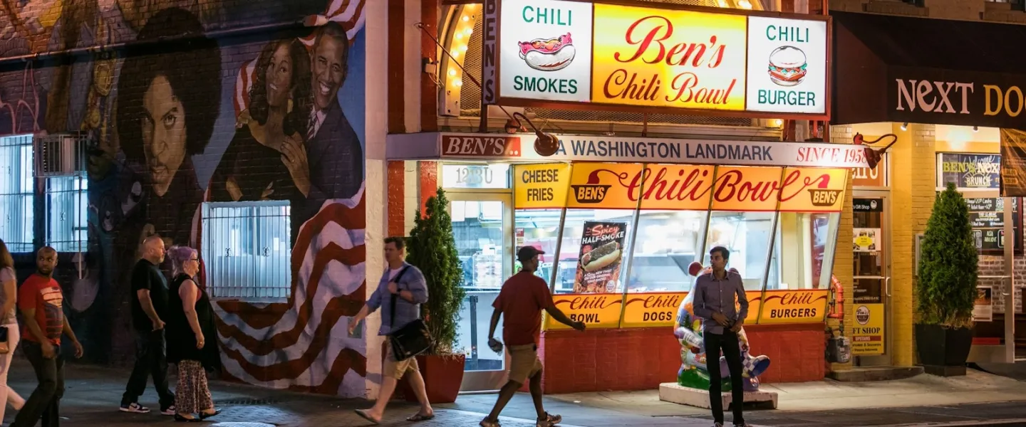 People walk by Ben's Chili Bowl at night. 