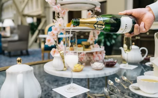 A hand pours champagne into a glass on a table set for a lavish high tea. 