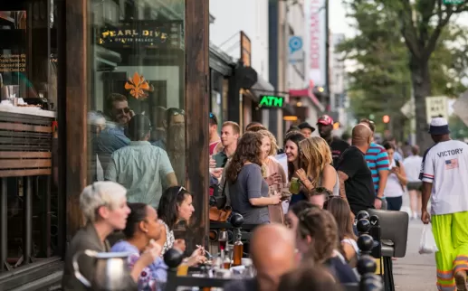  A lively crowd gathers outside Pearl Dive Oyster Palace, mingling and enjoying drinks along a bustling 14th Street sidewalk.
