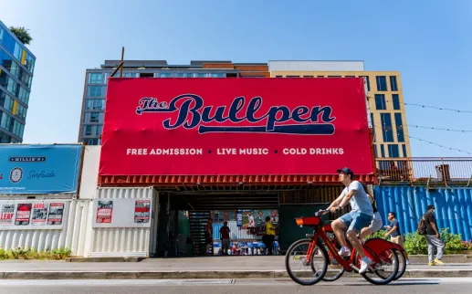 A cyclist rides past The Bullpen, an open-air venue near Nationals Park advertising live music, cold drinks and free admission.
