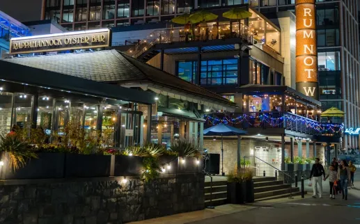 Businesses are lit up and busy at night along The Wharf in DC. 
