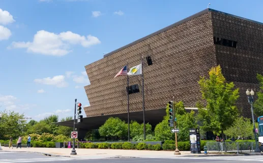 A view of the National Museum of African American History and Culture on a sunny day as cars pass by. . 