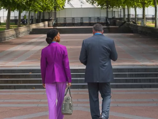 Two people walking on a brick sidewalk surrounded by green trees