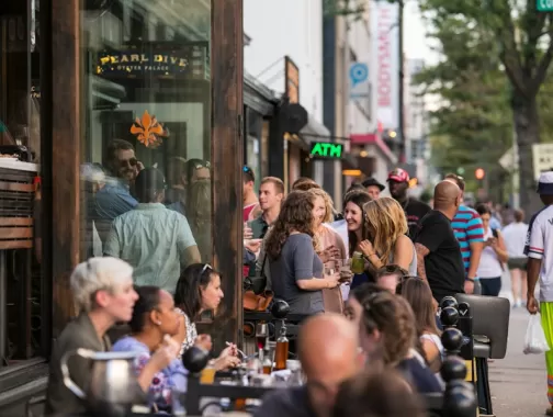  A lively crowd gathers outside Pearl Dive Oyster Palace, mingling and enjoying drinks along a bustling 14th Street sidewalk.