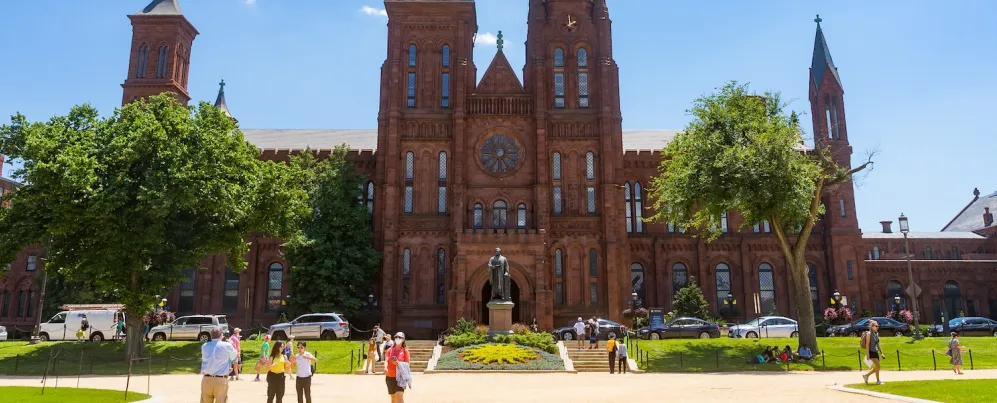 Visitors stroll across the sunny lawn in front of the iconic red sandstone Smithsonian Castle on the National Mall.